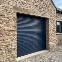 Porte de garage enroulable gris anthracite vue de l'extérieur sur une façade de maison en pierre