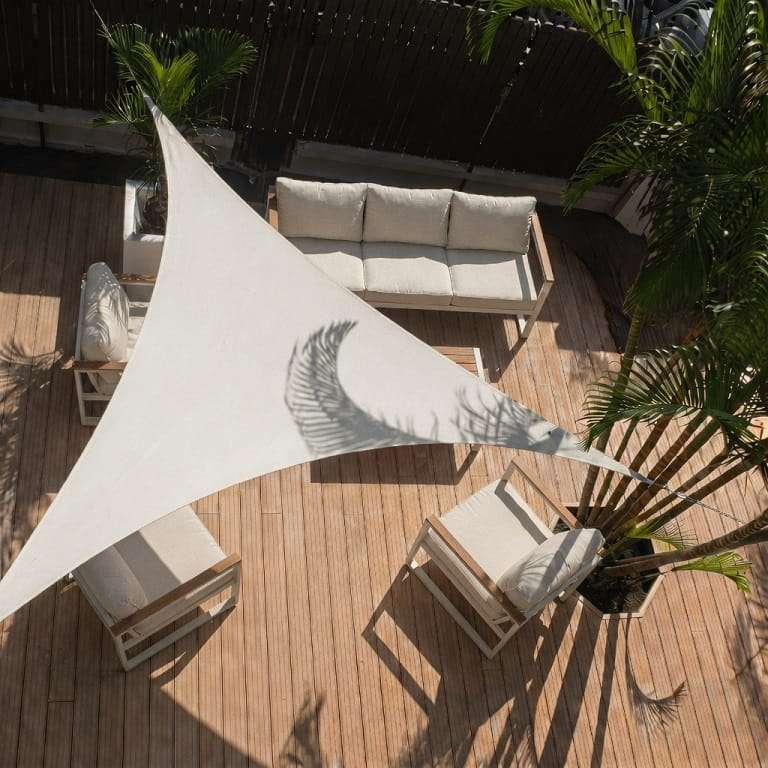 Voile d'ombrage triangulaire sable abritant un salon de jardin sur une terrasse arborée