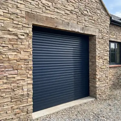 Porte de garage enroulable gris anthracite vue de l'extérieur sur une façade de maison en pierre