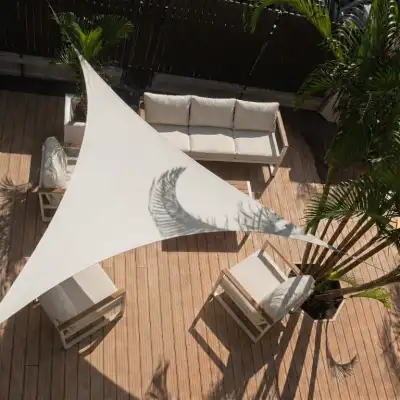 Voile d'ombrage triangulaire sable abritant un salon de jardin sur une terrasse arborée